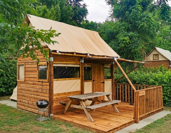 Vue extérieure de la tente lodge avec table de pique-nique, en location au camping **** du Lac Cormoranche dans l'Ain