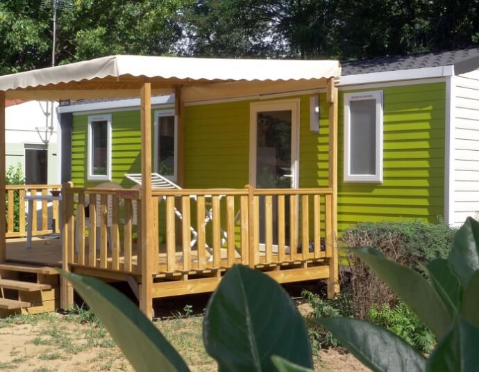 Vue extérieure du mobil-home 3 chambres avec terrasse couverte et un salon de jardin, en location au camping**** du lac de Cormoranche